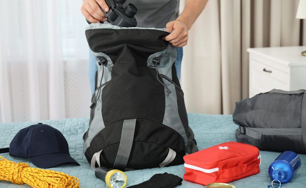 Man packing different camping equipment into backpack at home, closeup